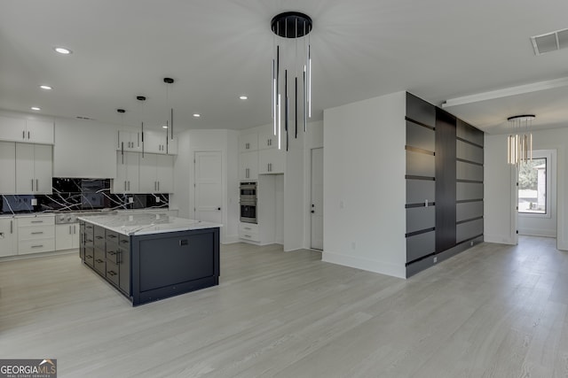 kitchen featuring backsplash, a center island with sink, pendant lighting, white cabinetry, and light stone counters