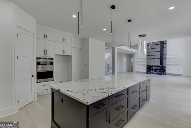 kitchen with white cabinetry, light hardwood / wood-style flooring, hanging light fixtures, double oven, and light stone counters