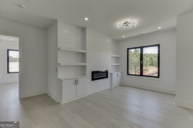 unfurnished living room featuring a large fireplace, light hardwood / wood-style flooring, and built in shelves