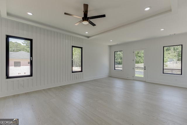 spare room with ceiling fan, a tray ceiling, light hardwood / wood-style flooring, and a healthy amount of sunlight