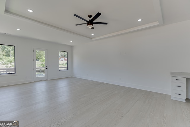 empty room featuring ceiling fan, light hardwood / wood-style flooring, and a tray ceiling