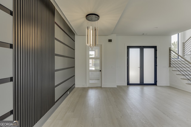 empty room featuring french doors, a chandelier, and light hardwood / wood-style flooring