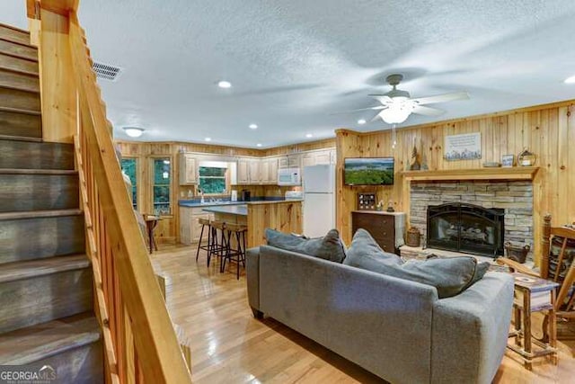 living room featuring light hardwood / wood-style floors, wood walls, ceiling fan, a fireplace, and a textured ceiling