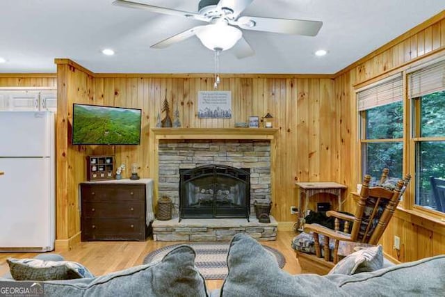 living room featuring ceiling fan, a wealth of natural light, wooden walls, and a fireplace