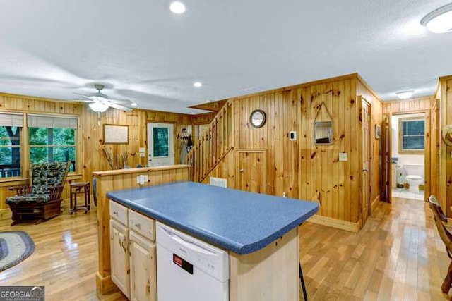 kitchen featuring light hardwood / wood-style floors, wooden walls, ceiling fan, dishwasher, and a kitchen island