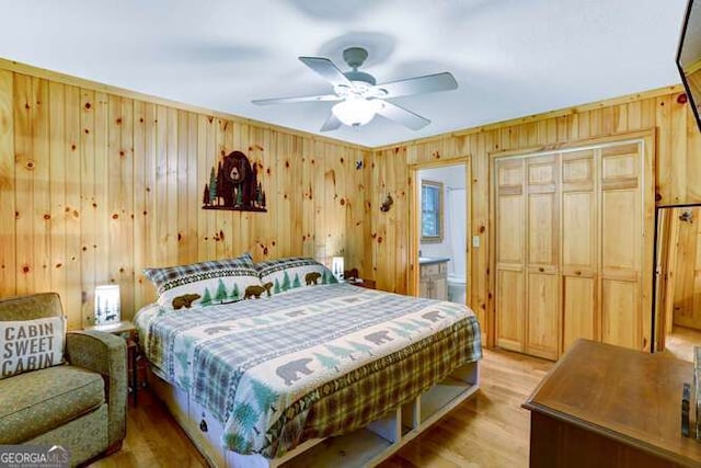 bedroom with ceiling fan, ensuite bathroom, light hardwood / wood-style floors, wooden walls, and a closet