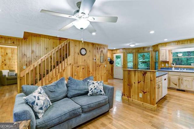 living room with ceiling fan, wooden walls, and light hardwood / wood-style floors