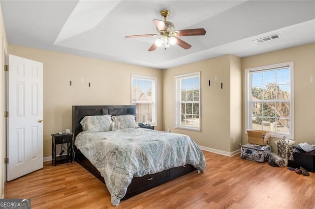 bedroom featuring ceiling fan, a tray ceiling, multiple windows, and hardwood / wood-style flooring