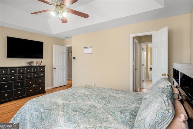 bedroom with light wood-type flooring, ceiling fan, and a raised ceiling