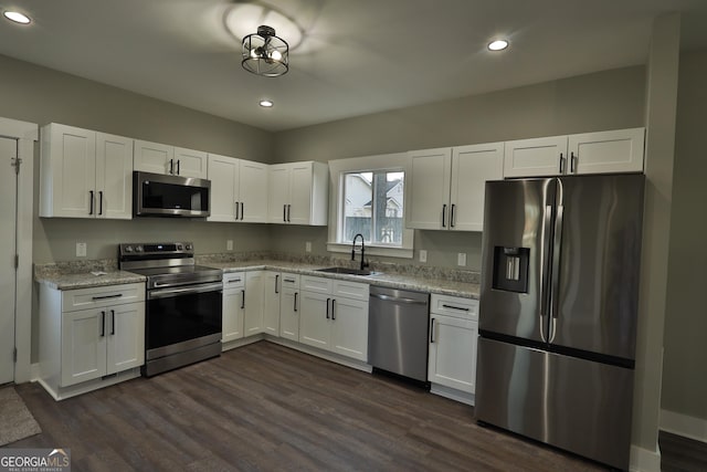 kitchen with sink, appliances with stainless steel finishes, dark hardwood / wood-style floors, light stone countertops, and white cabinets