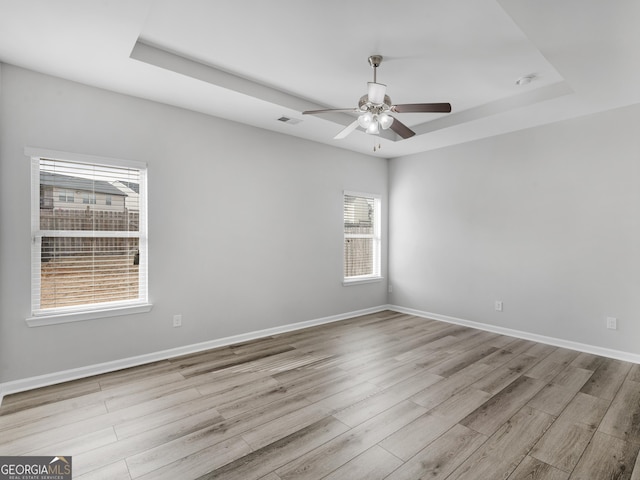 unfurnished room with ceiling fan, a tray ceiling, and light wood-type flooring