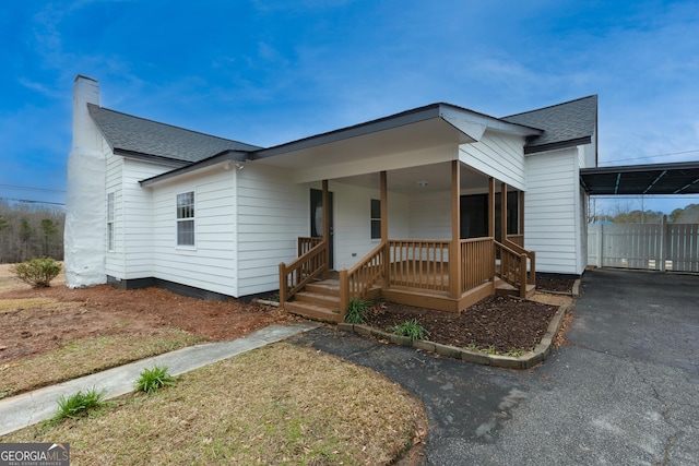 view of front of house featuring aphalt driveway, a shingled roof, fence, a carport, and a chimney