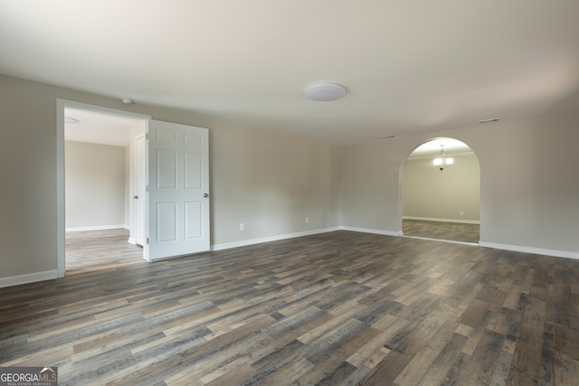 unfurnished room with dark wood-type flooring, arched walkways, and baseboards