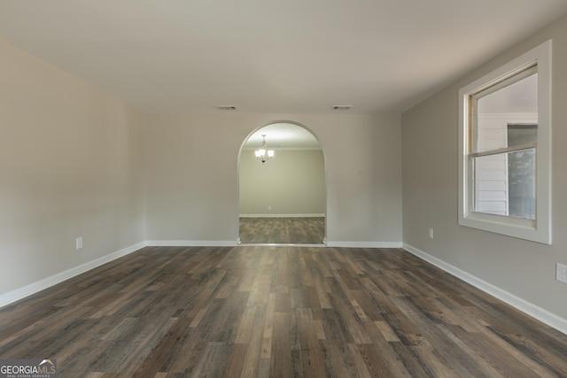 unfurnished room featuring arched walkways, dark wood-type flooring, visible vents, and baseboards