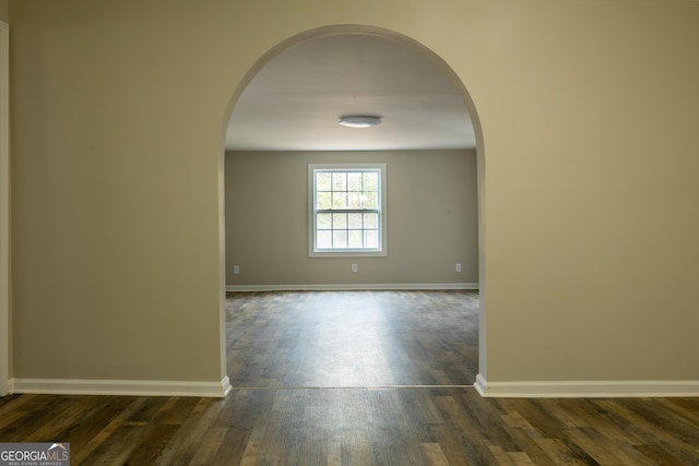 empty room with arched walkways, dark wood-style flooring, and baseboards