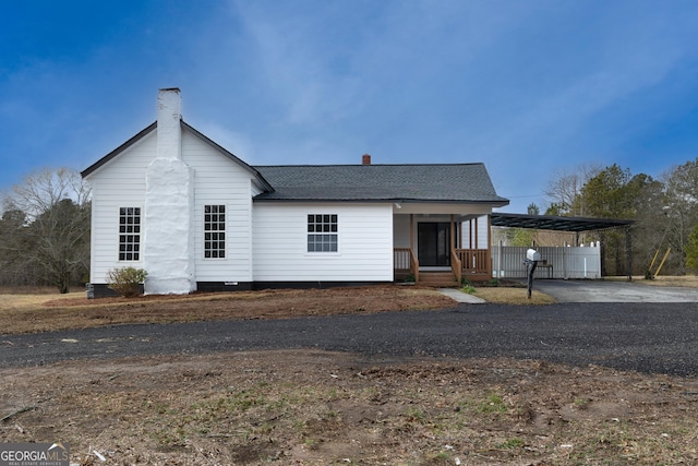 view of front of house featuring a porch, aphalt driveway, a shingled roof, a carport, and a chimney