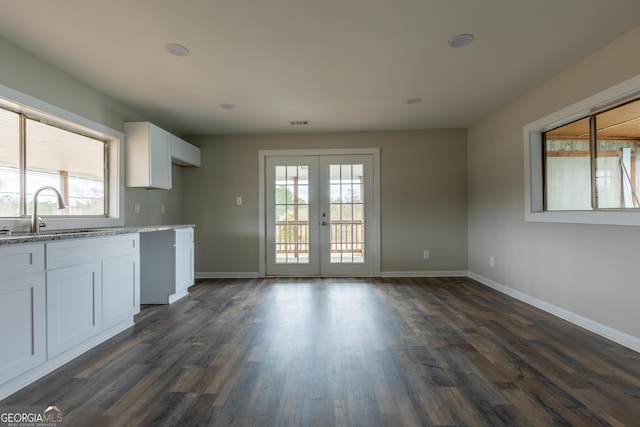 kitchen featuring baseboards, white cabinets, light stone countertops, french doors, and a sink