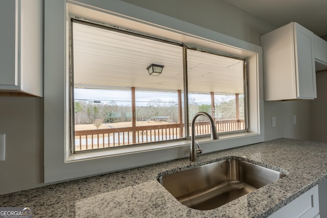 kitchen with a sink, white cabinetry, and light stone countertops