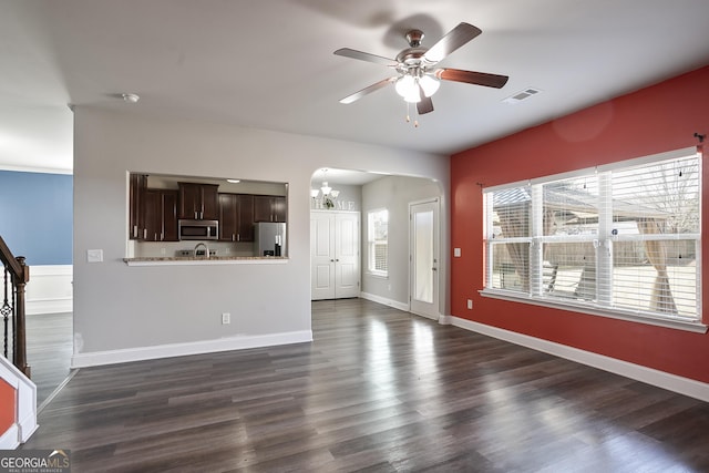 unfurnished living room featuring dark wood-type flooring, sink, and ceiling fan with notable chandelier