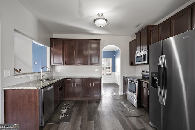 kitchen featuring stainless steel appliances, dark wood-type flooring, light stone countertops, dark brown cabinetry, and sink