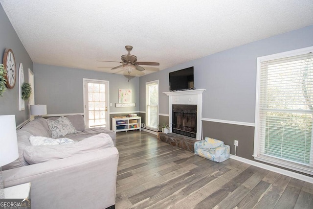 living room featuring dark wood-type flooring, ceiling fan, a fireplace, and a textured ceiling