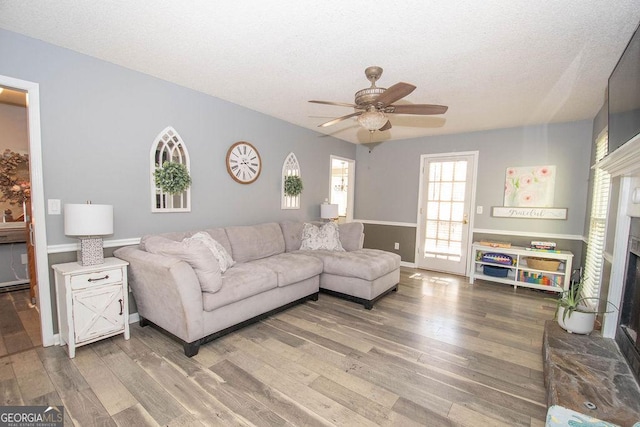 living room featuring ceiling fan, a textured ceiling, hardwood / wood-style flooring, and a fireplace