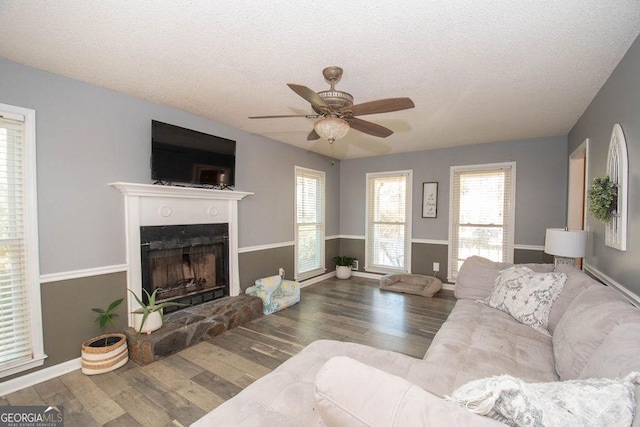 living room with ceiling fan, wood-type flooring, a textured ceiling, and a stone fireplace