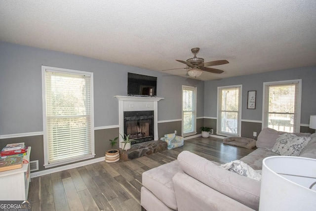 living room with ceiling fan, plenty of natural light, a fireplace, wood-type flooring, and a textured ceiling