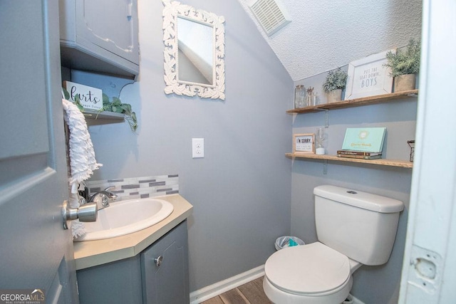 bathroom with a textured ceiling, lofted ceiling, vanity, backsplash, and toilet