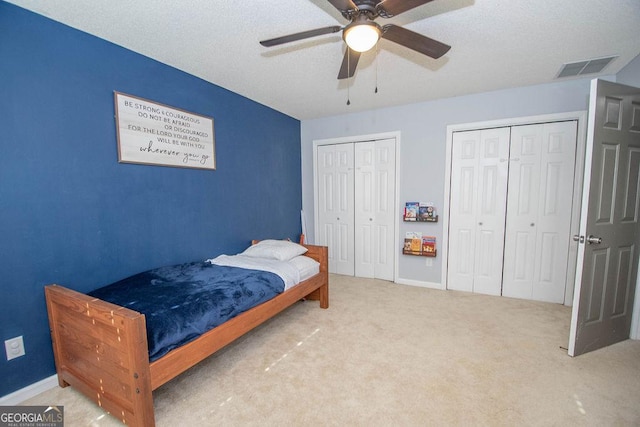 carpeted bedroom with ceiling fan, multiple closets, and a textured ceiling