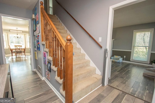 stairway with an inviting chandelier, a textured ceiling, and hardwood / wood-style floors