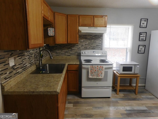 kitchen with tasteful backsplash, white appliances, light wood-type flooring, light stone countertops, and sink