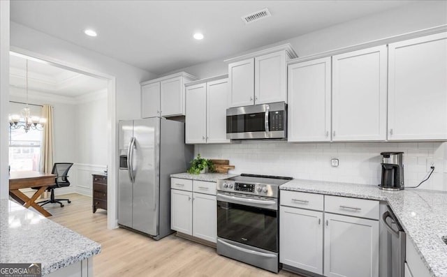 kitchen with appliances with stainless steel finishes, white cabinetry, tasteful backsplash, and a notable chandelier