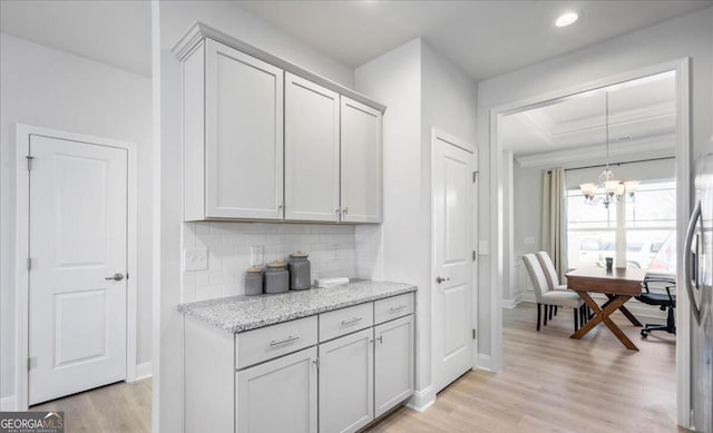 kitchen featuring decorative backsplash, light wood-type flooring, hanging light fixtures, light stone countertops, and a chandelier