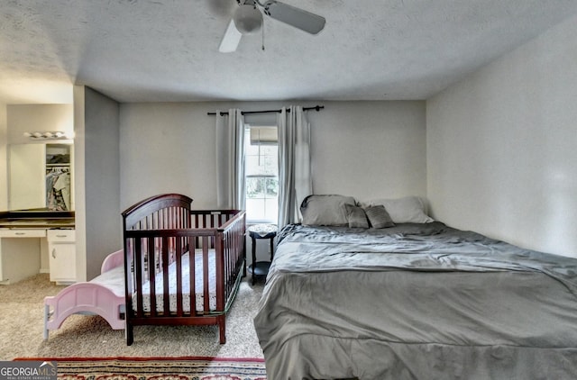 carpeted bedroom featuring connected bathroom, a textured ceiling, built in desk, and ceiling fan