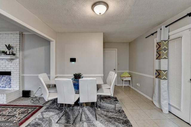 dining area featuring light tile patterned floors, a textured ceiling, and a brick fireplace