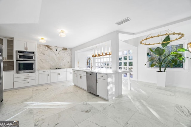 kitchen with white cabinets, appliances with stainless steel finishes, an island with sink, decorative backsplash, and sink