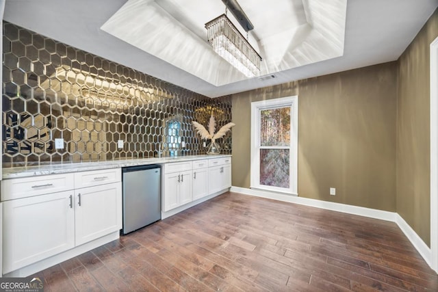 kitchen featuring dark hardwood / wood-style floors, a raised ceiling, refrigerator, white cabinets, and light stone counters