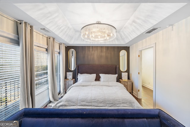 bedroom with a raised ceiling, a chandelier, and hardwood / wood-style flooring