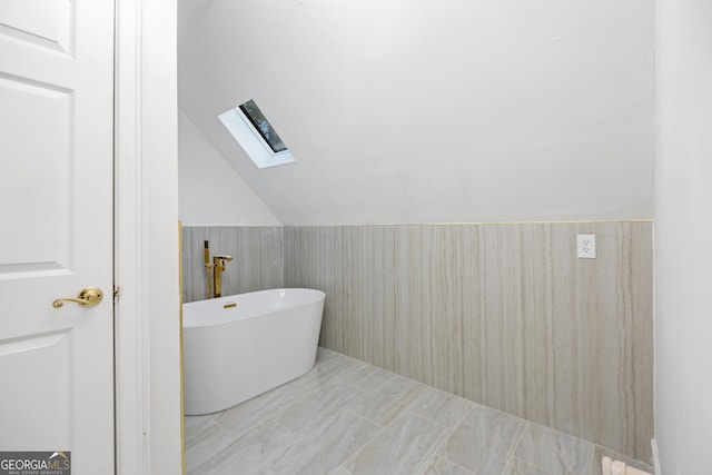 bathroom with tile patterned flooring, lofted ceiling with skylight, and a bathing tub