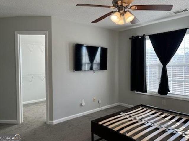 unfurnished bedroom with dark colored carpet, a spacious closet, ceiling fan, and a textured ceiling