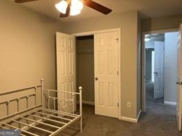 unfurnished bedroom with ceiling fan, a closet, and dark colored carpet