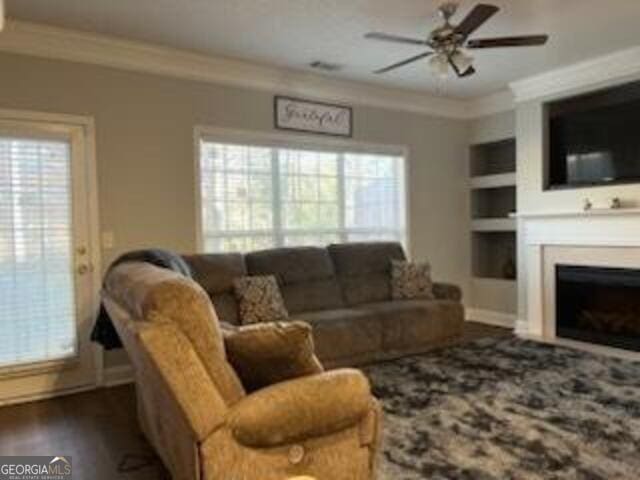 living room featuring crown molding, ceiling fan, dark wood-type flooring, and built in features