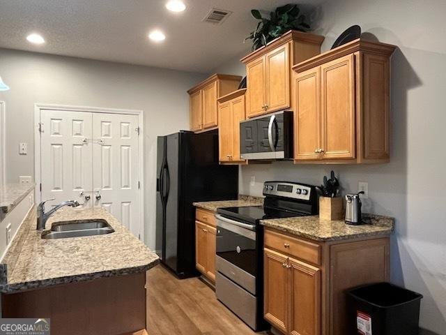 kitchen featuring light stone counters, sink, light hardwood / wood-style flooring, and appliances with stainless steel finishes