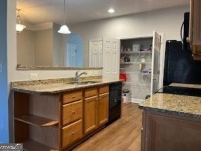 kitchen with decorative light fixtures, dishwasher, sink, light stone counters, and light hardwood / wood-style floors