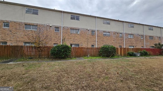 rear view of property with brick siding, fence, and a lawn