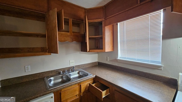 kitchen with open shelves, brown cabinetry, dark countertops, and a sink