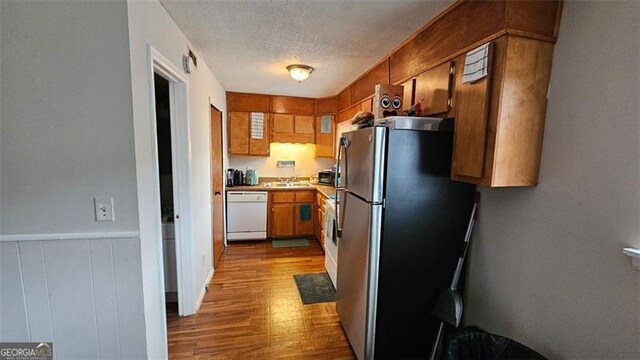 kitchen featuring a textured ceiling, dishwasher, sink, stainless steel fridge, and light hardwood / wood-style flooring