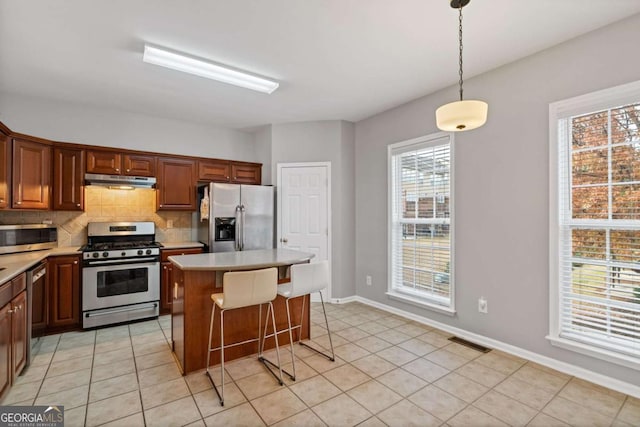 kitchen with a center island, decorative backsplash, light tile patterned flooring, hanging light fixtures, and appliances with stainless steel finishes