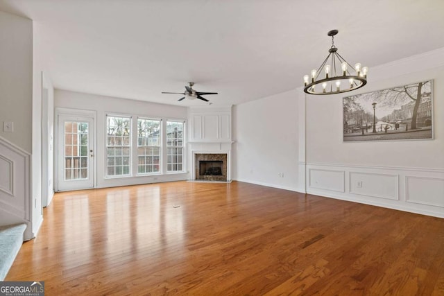 unfurnished living room featuring ceiling fan with notable chandelier, light hardwood / wood-style floors, ornamental molding, and a premium fireplace